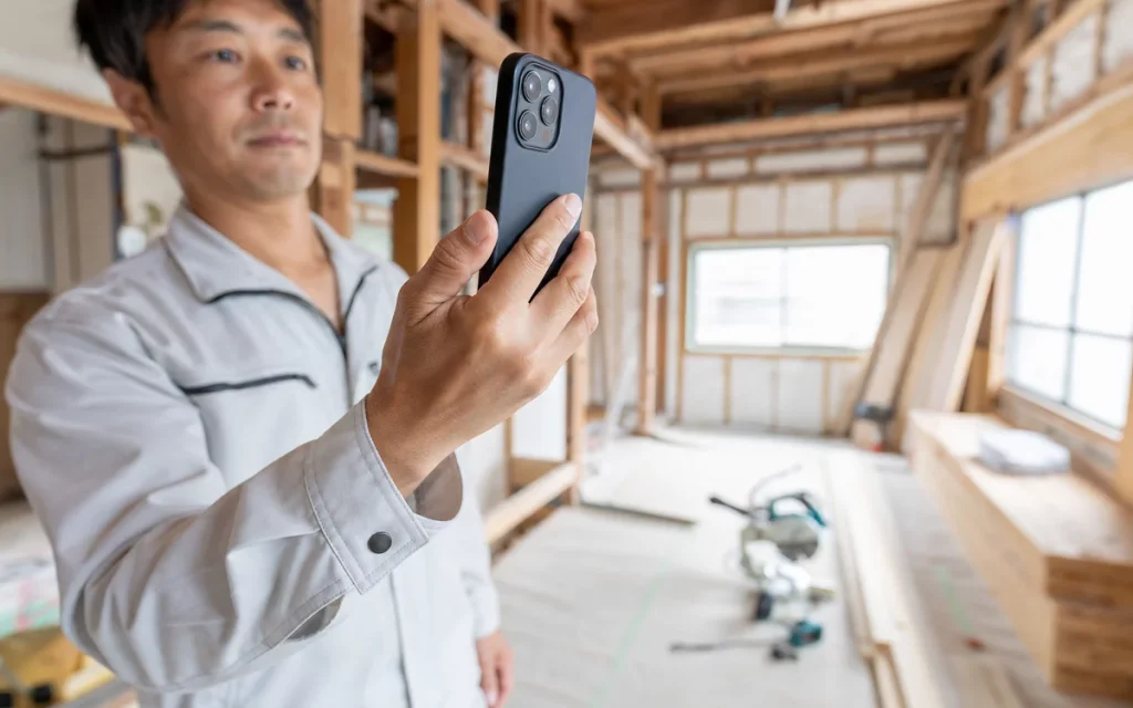 改装中の木造現場でスマートフォンを使い施工箇所を撮影する作業員