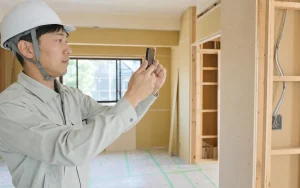改装中の住宅の室内でスマートフォンを構えて工事写真を撮影する現場監督